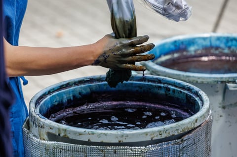 A droplet of blue dye falls from a tanned hand
