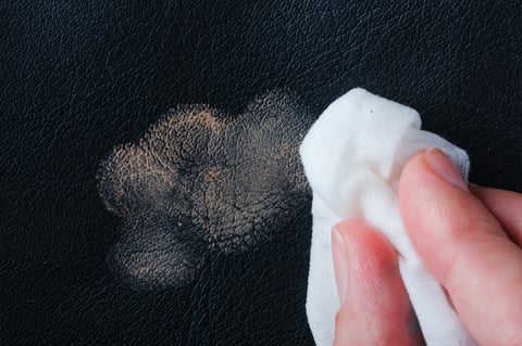 A hand wiping cosmetic stain from dark leather material