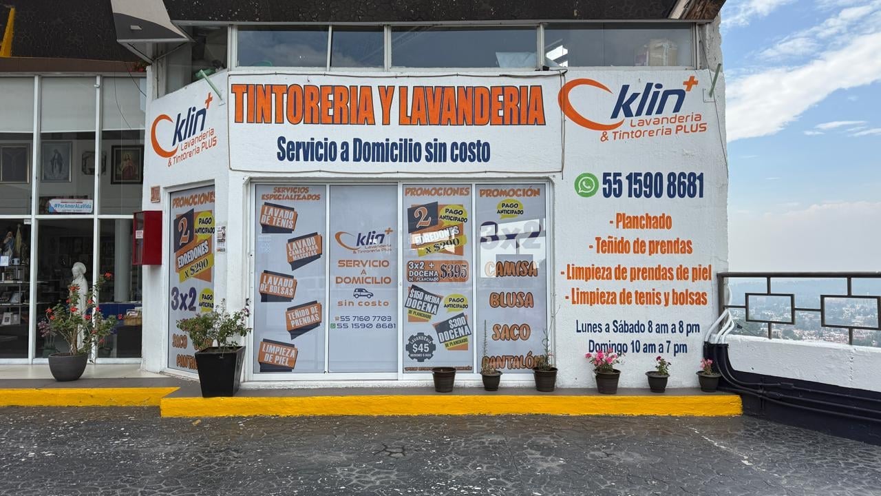 Storefront of a laundromat and dry cleaning service with signage advertising home delivery phone number and hours of operation